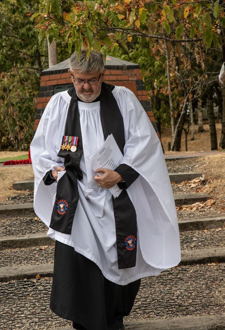 The padre in white surplice and black scarf, wearing medals