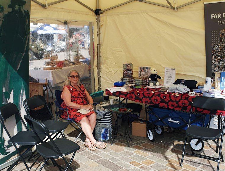 Jill Robertson seated at the COFEPOW stall in a marquee, with merchandise and poppy displays