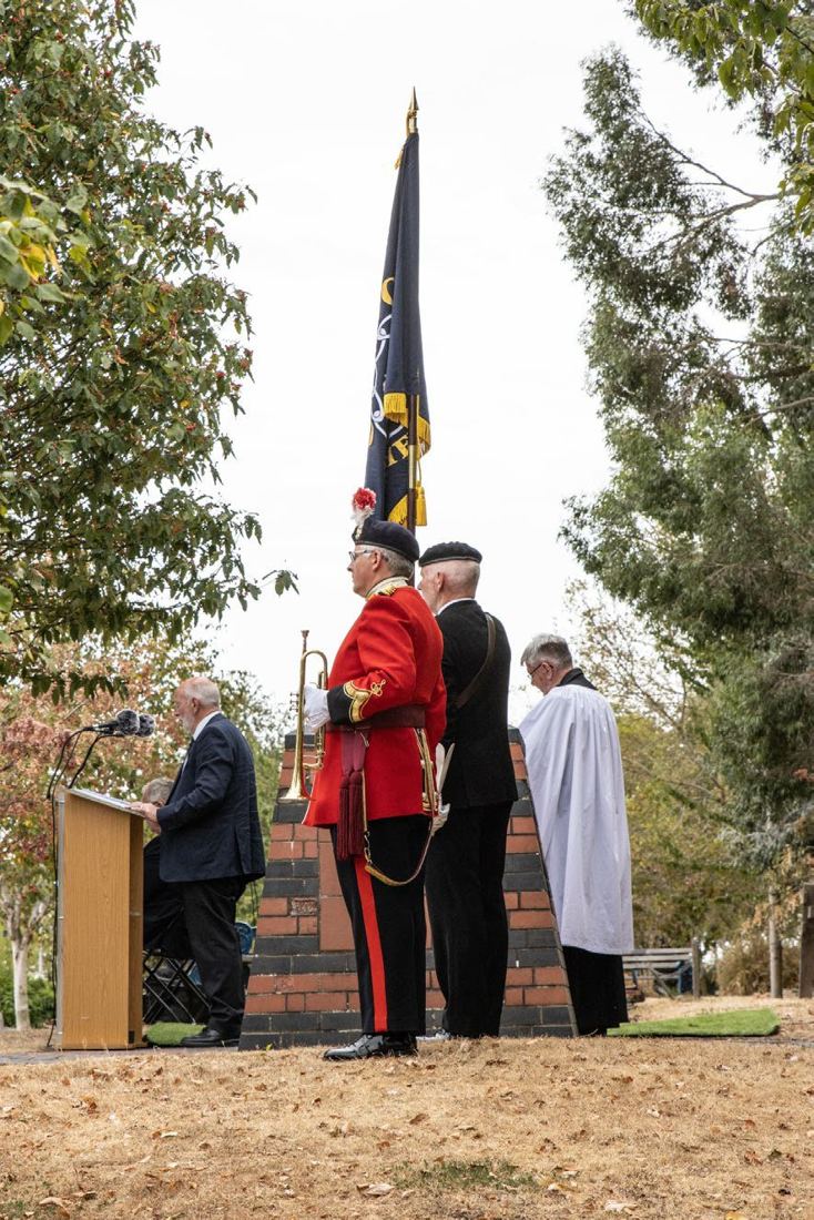 A bugler in red ceremonial uniform beside the memorial during the service