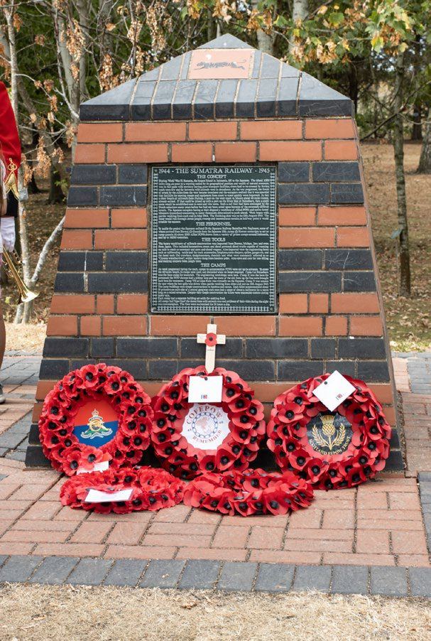 Poppy wreaths laid at the foot of a brick memorial with an inscribed plaque